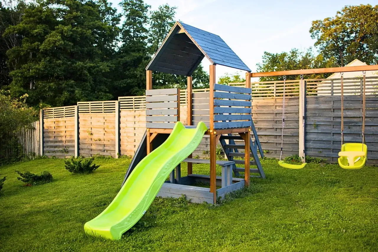 Nowy domek dla dzieci projekt: zjeżdżalnia, huśtawki i piaskownica na zielonym trawniku.