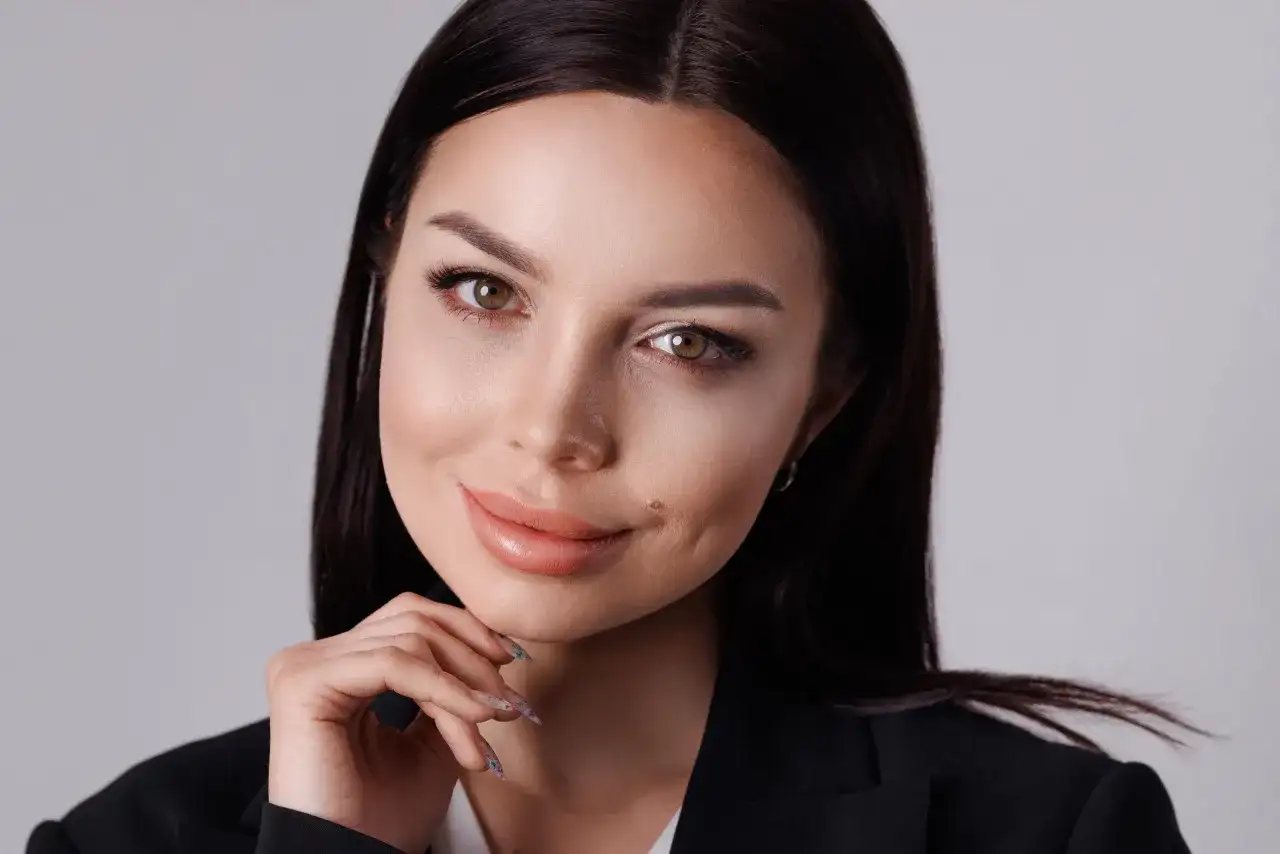 Elegancka kobieta w czarnej marynarce, opierająca podbródek na dłoni, pozuje w studiu.