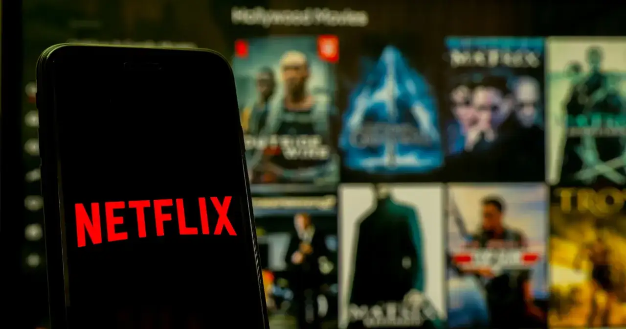 Telefon z logo Netflix na tle ekranu z filmami. Zastanawiasz się, co obejrzeć na Netflixie?
