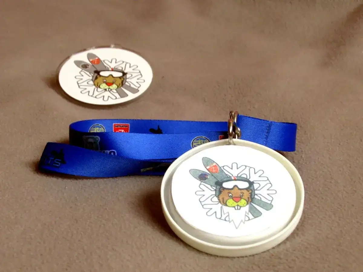 Jak zrobić medal dla dziecka? Dwa okrągłe medale z bobrem narciarzem i niebieska wstążka.