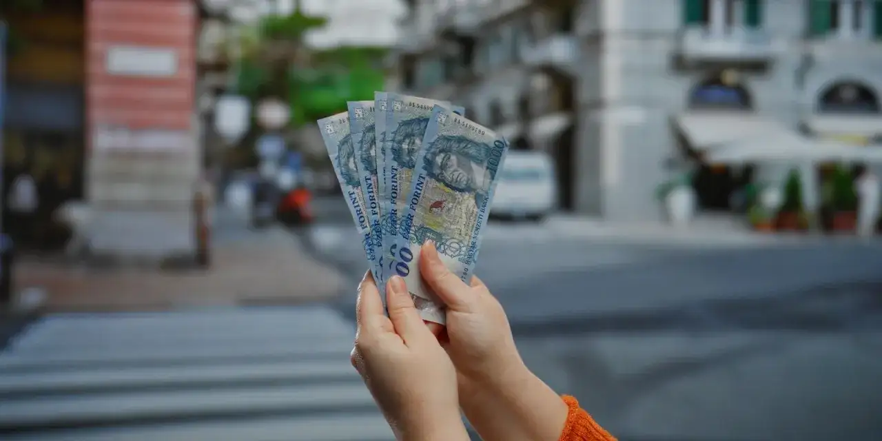 Ręce trzymające banknoty 1000 forintów. Zastanawiasz się, ile kosztuje chleb na Węgrzech?