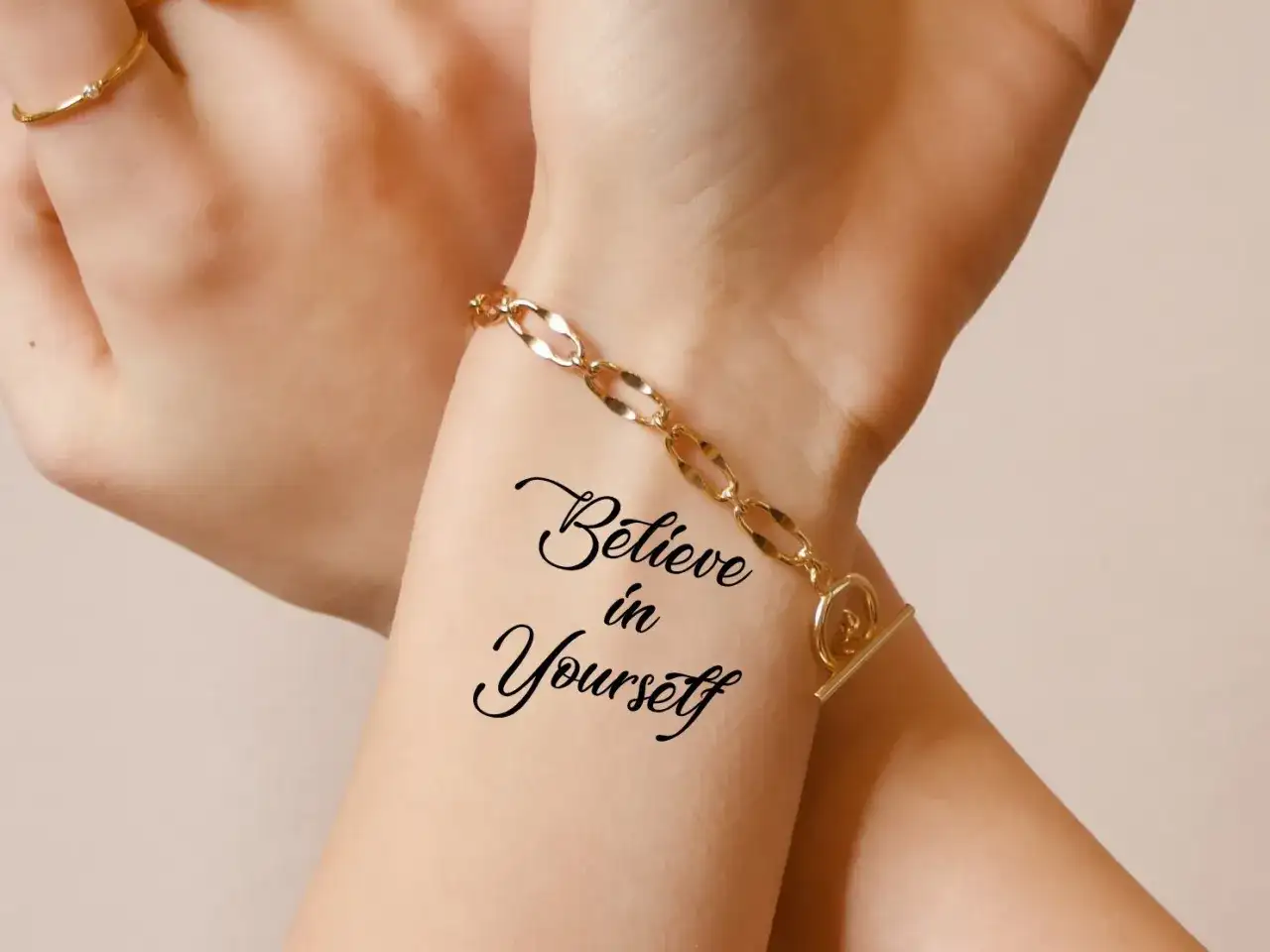 Dłoń z tatuażem "Believe in Yourself" i złotą bransoletką.