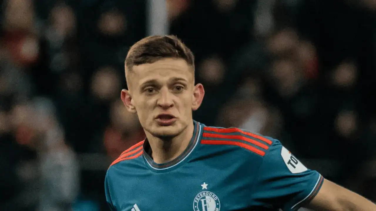 Młody piłkarz w niebieskiej koszulce z czerwonymi pasami na ramionach, z emblematem Feyenoordu. Czy to **kitman, kto to**?