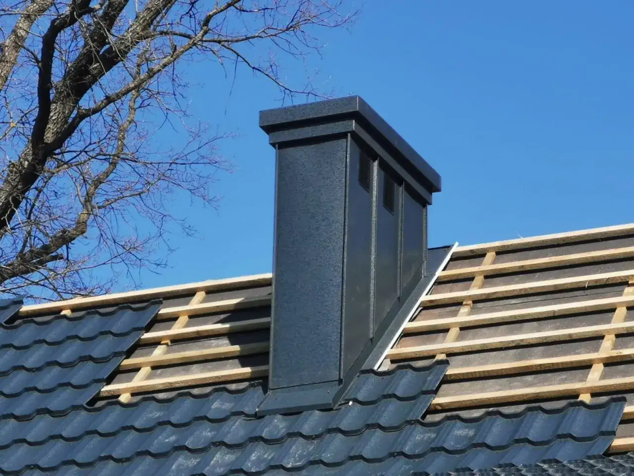 Nowy komin na dachu, widoczne łaty i kontrłaty pod dachówką.