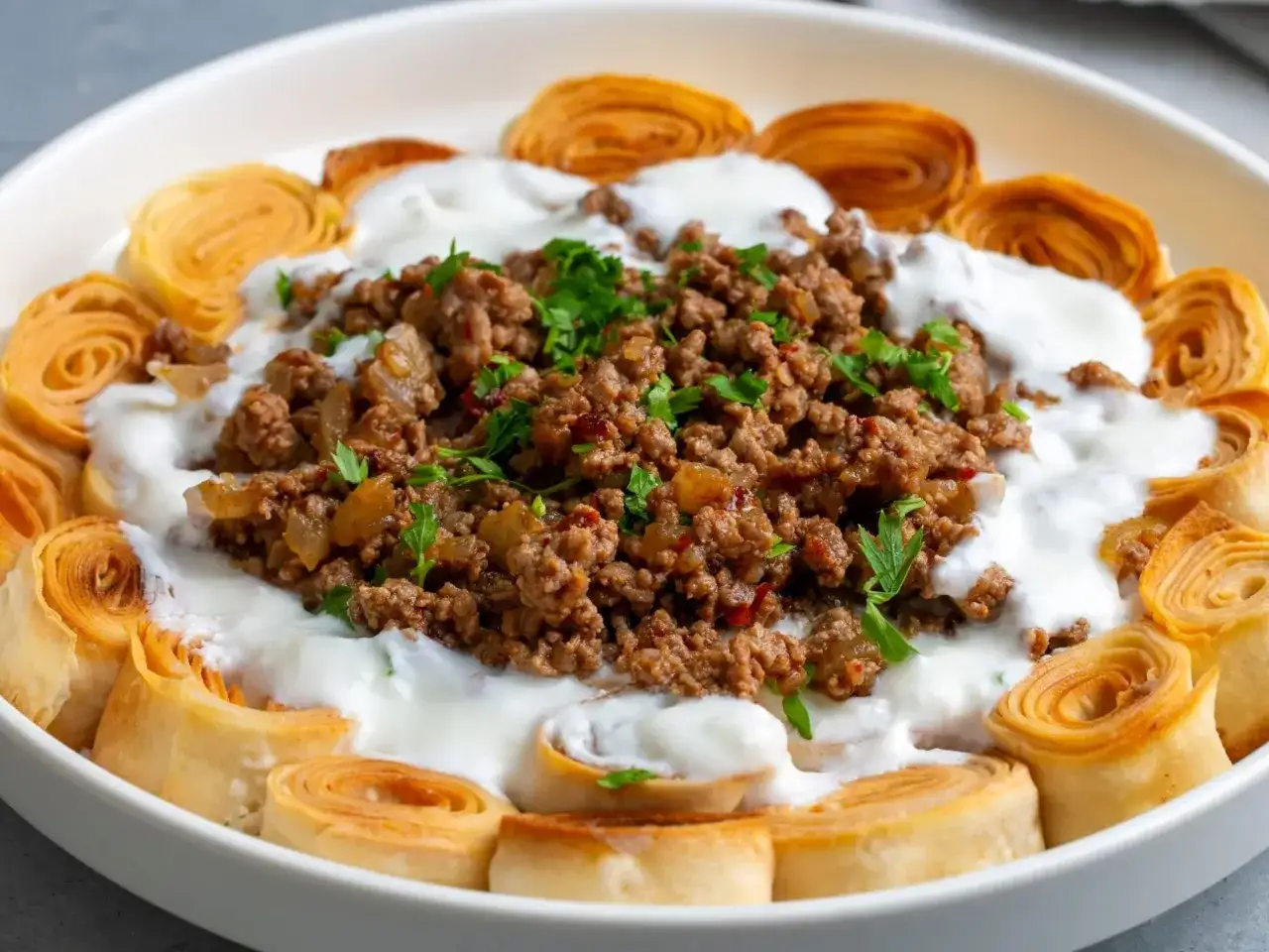 Danie z mielonej wołowiny, jogurtu i roladek z ciasta filo, posypane natką pietruszki.