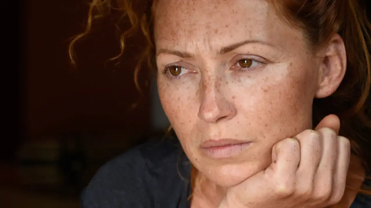 Portret kobiety z piegami, zamyślonej, z dłonią podpartą na policzku. Może odzwierciedlać 24 cechy wysoko wrażliwych osób.