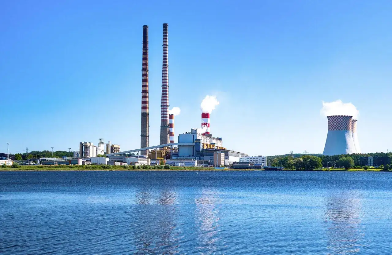 Elektrownia z kominami i chłodniami, odbijająca się w wodzie.