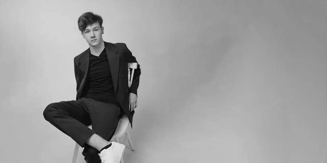 Młody mężczyzna w marynarce i t-shircie, siedzący na krześle. Stylowe zdjęcie profilowe męskie.