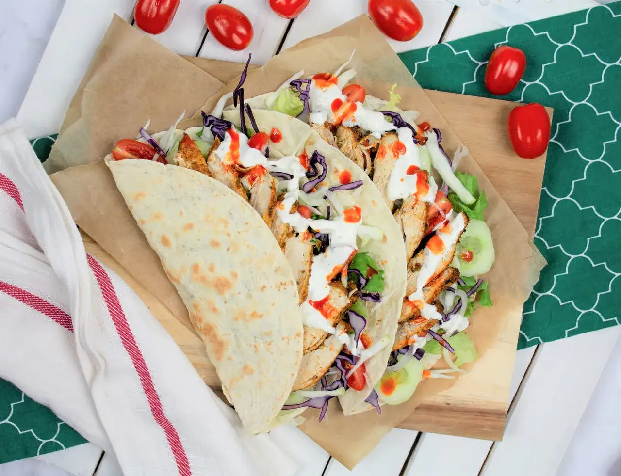 Kebab w tortilli z kurczakiem, warzywami i sosami, obok pomidorki.