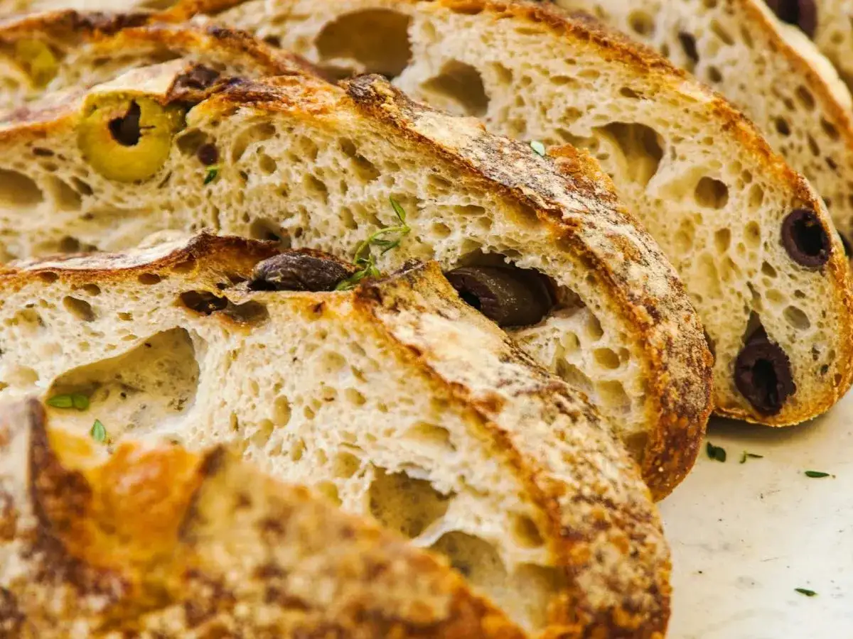 Kromki chleba z oliwkami i ziołami. Miękki, lekko wilgotny środek wygląda apetycznie, więc można jeść.