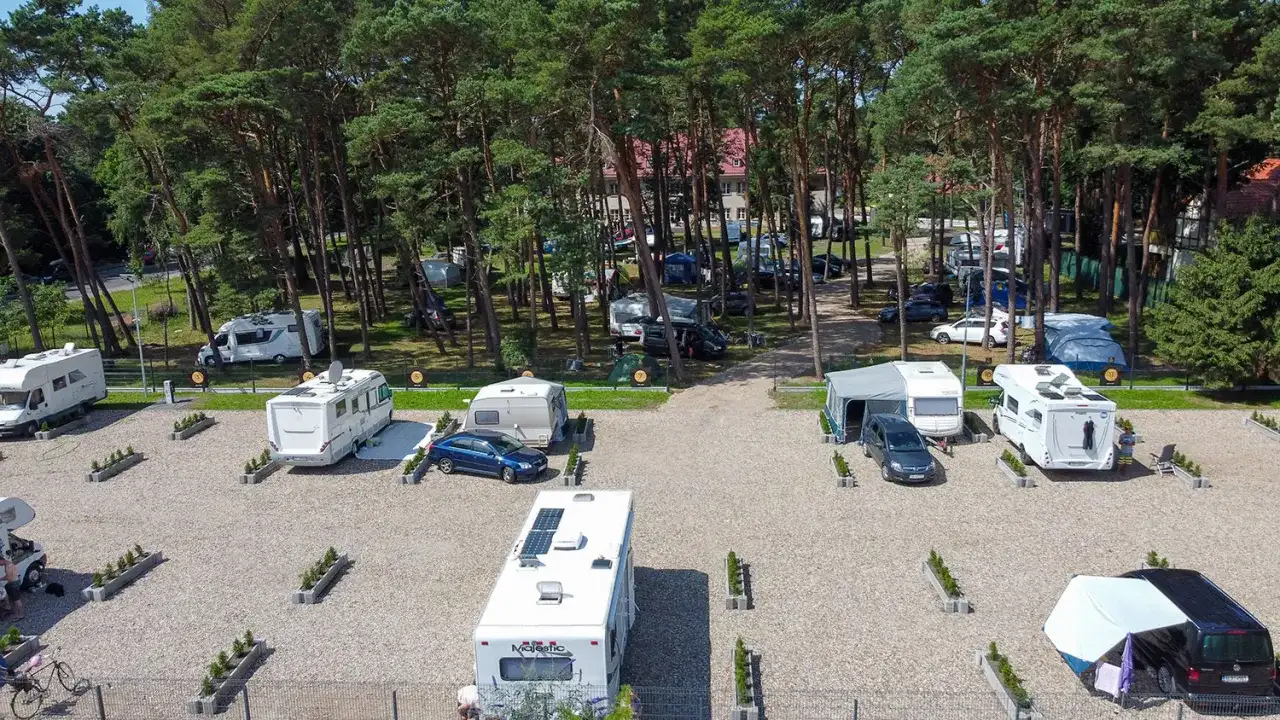 Kampery i przyczepy kempingowe na żwirowym polu namiotowym w lesie sosnowym. Widok z lotu ptaka na sea camp Rogowo.