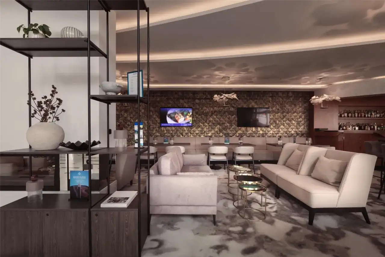 Nowoczesny salon hotelowy z sofami, stolikami i barem w tle.