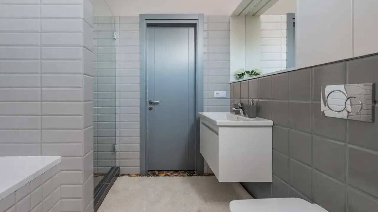 Nowoczesna łazienka z szarymi i białymi kafelkami, umywalką i drzwiami.