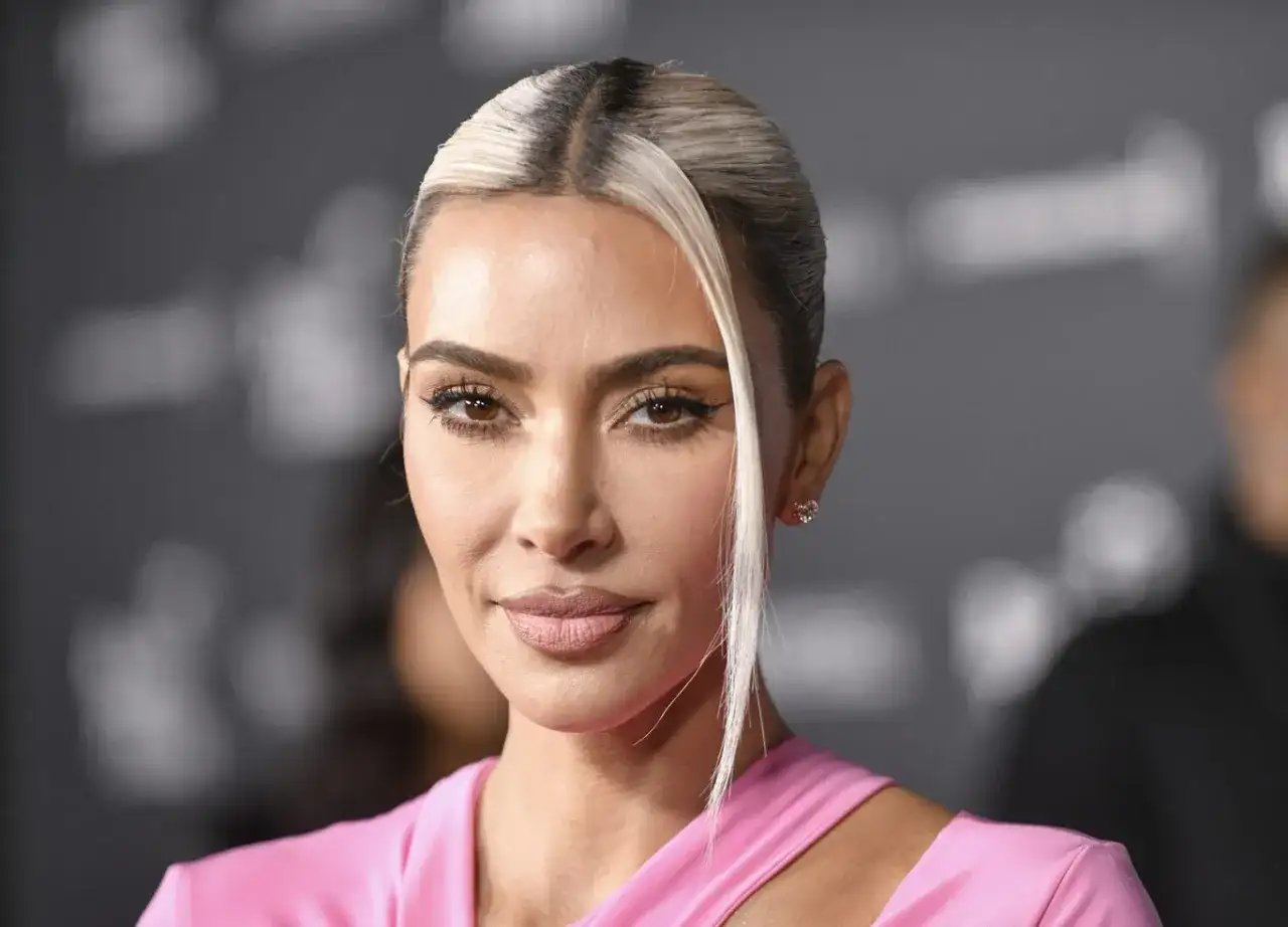 Kim Kardashian w różowej sukience, z blond pasmem włosów opadającym na twarz. Jej spojrzenie idealnie pasuje do jej stylu na Instagramie.