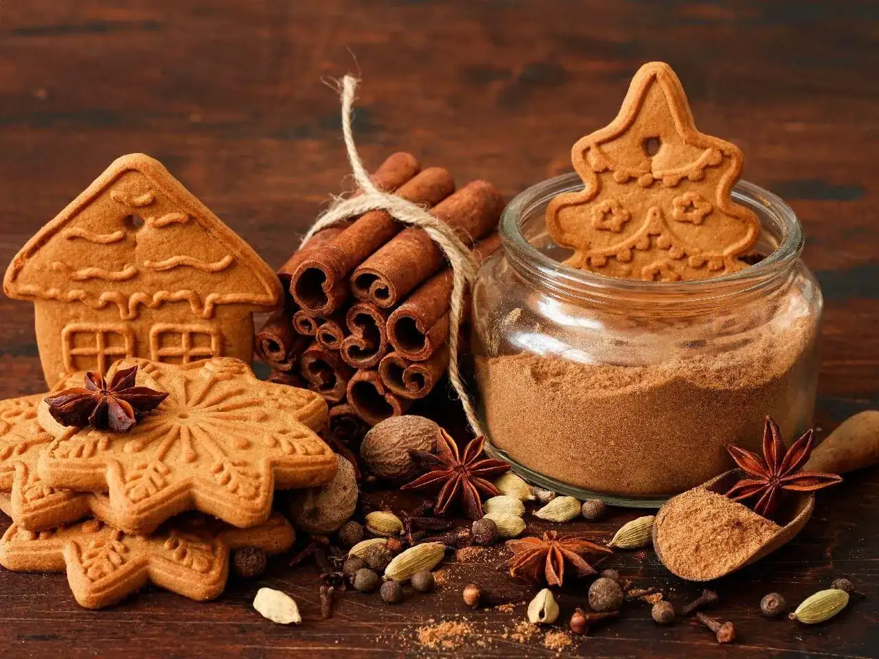 Pierniczki w kształcie domu i gwiazdek, laska cynamonu, słoik z przyprawą i przyprawy korzenne.