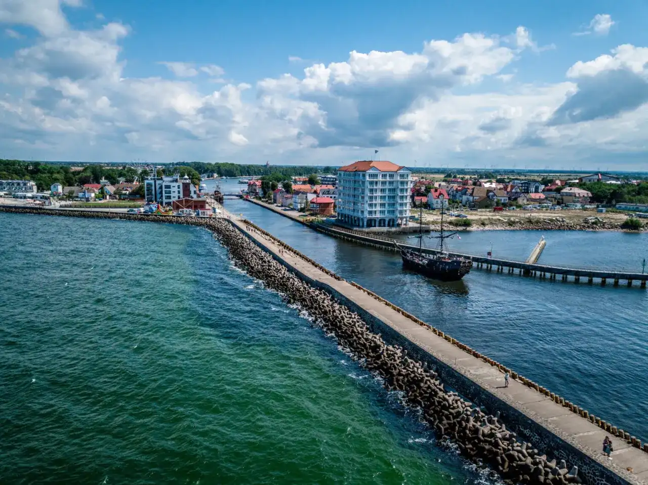 Port w Darłowie z falochronem, statkiem pirackim i nowoczesnym budynkiem. Atrakcje turystyczne na wyciągnięcie ręki.