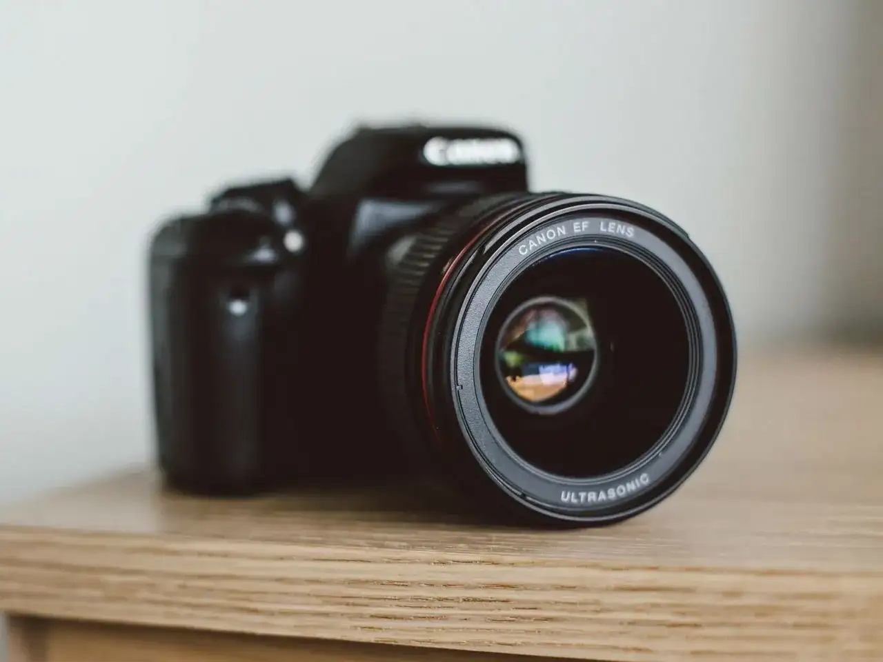 Czarna lustrzanka Canon z obiektywem EF LENS ULTRASONIC na drewnianym blacie.