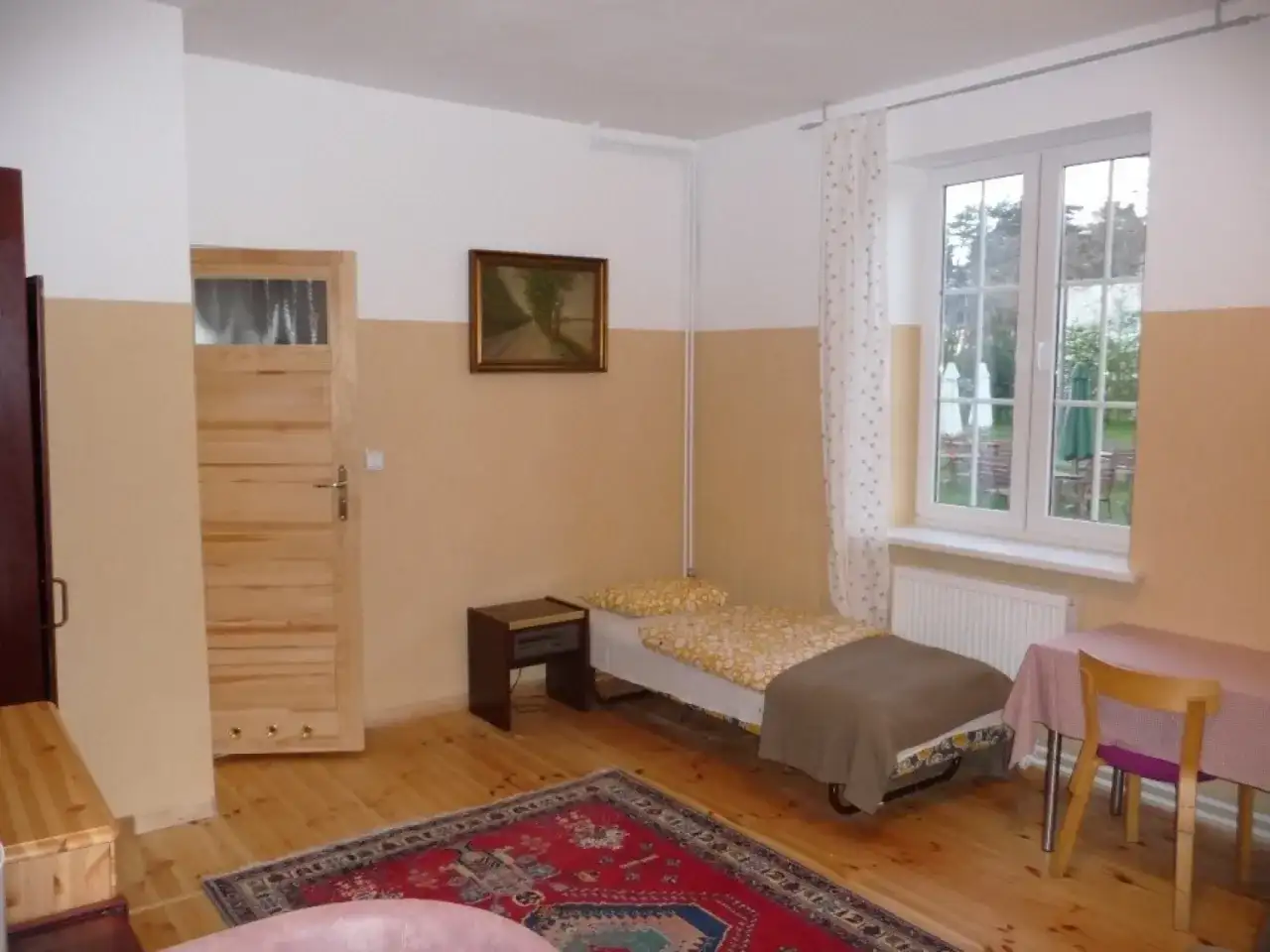 Pokój z łóżkiem, szafką nocną, drzwiami, oknem i dywanem.