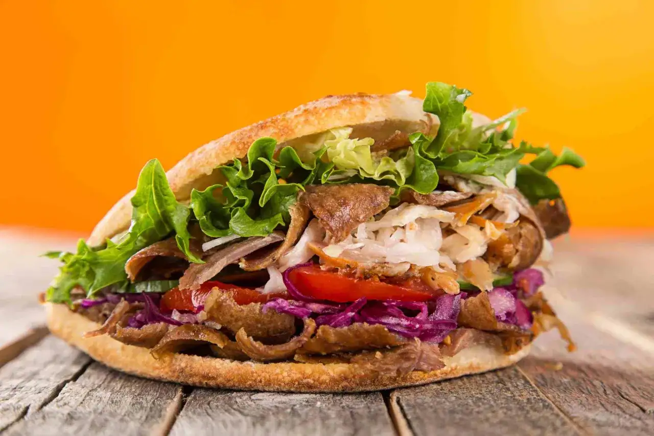 Kebab w bułce z mięsem, warzywami i sałatą na drewnianym stole.