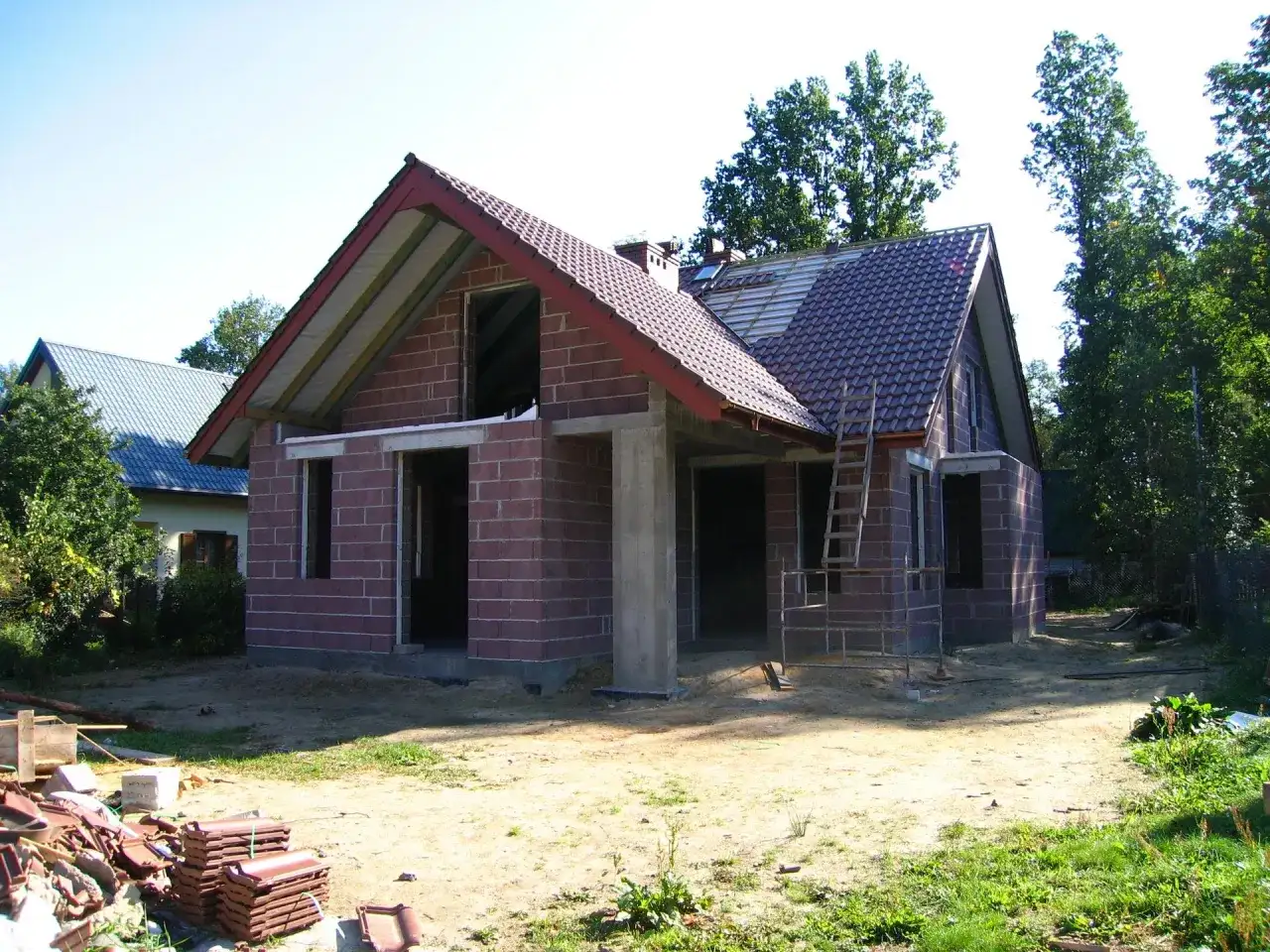 Budowa domu w toku, widoczne materiały budowlane i drabina. Może to być podstawa do obliczenia kary za samowolę budowlaną.