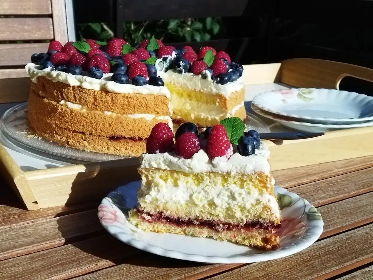 Tort biszkoptowy z kremem, malinami i borówkami, udekorowany miętą.