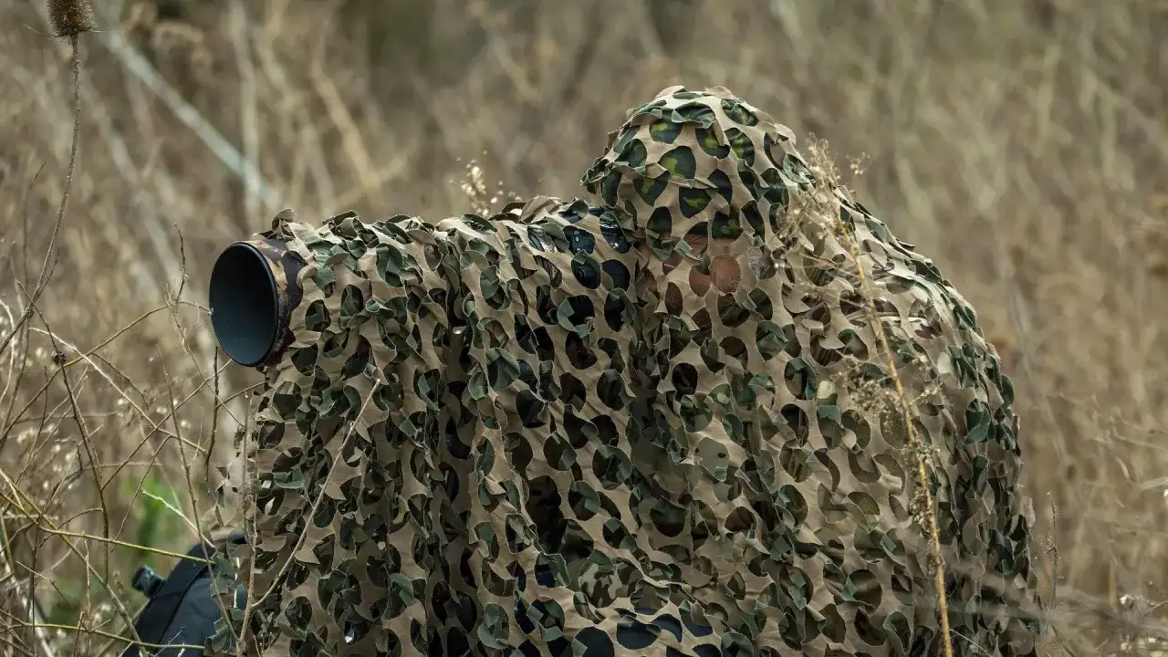 Fotografia przyrodnicza: ukryty fotograf z aparatem w kamuflażu czeka na idealny kadr wśród suchych traw.