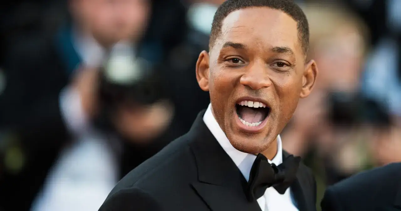 Will Smith w czarnym smokingu z muszką, uśmiecha się szeroko. Ciekawe, ile lat ma Will Smith, patrząc na jego energię!