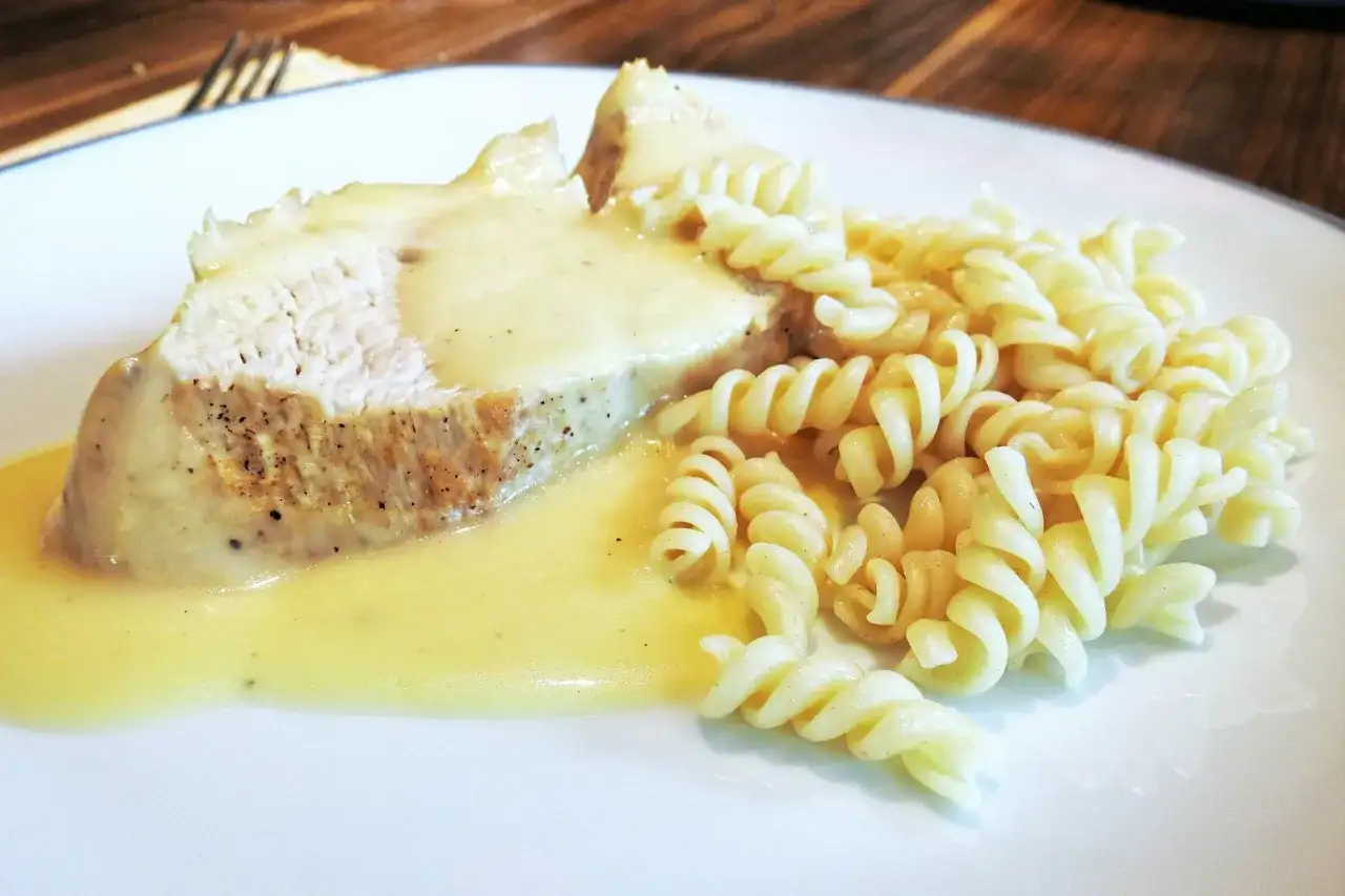 Kawałek mięsa w sosie z makaronem fusilli na białym talerzu.