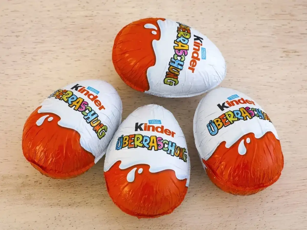 Cztery jajka Kinder Niespodzianka w pomarańczowo-białych opakowaniach na drewnianym tle.