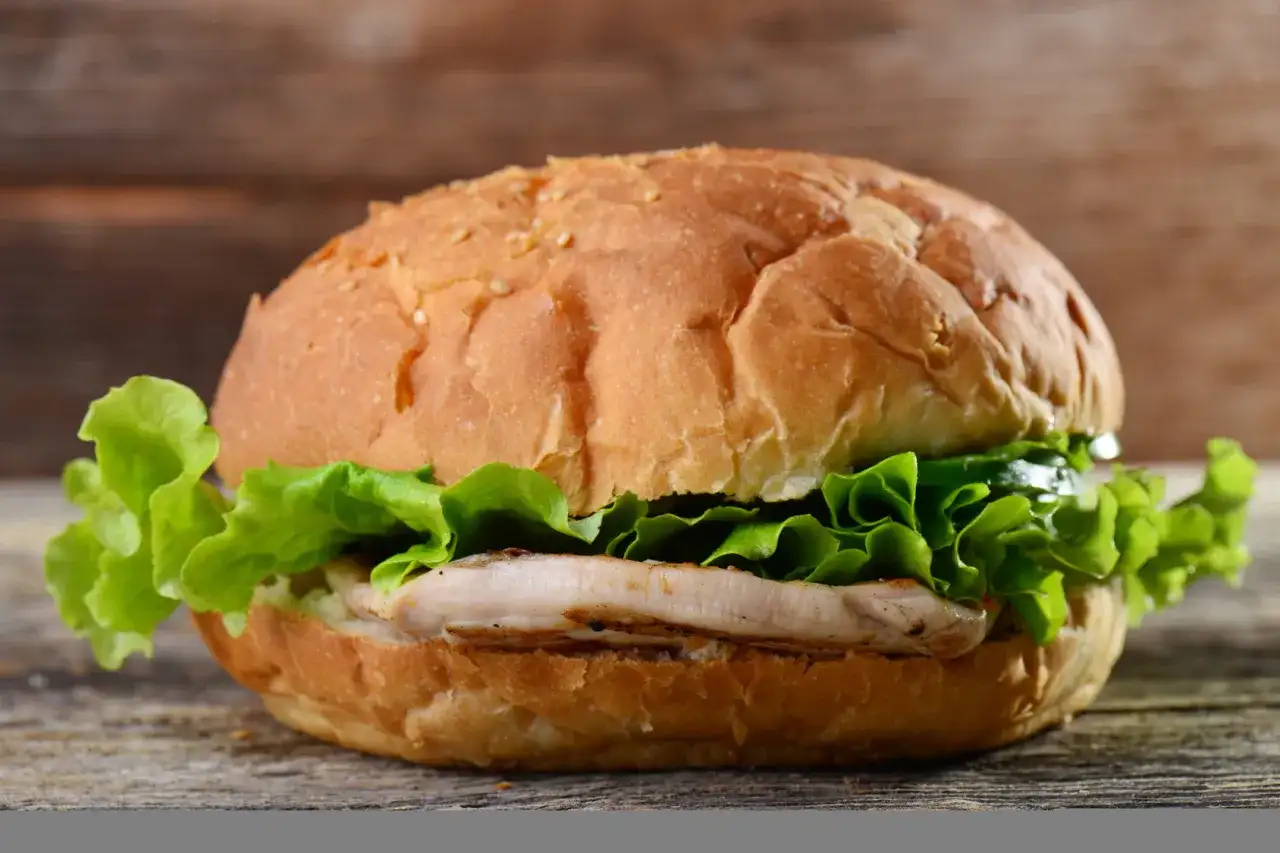 Burger z kurczakiem i sałatą na drewnianym tle.
