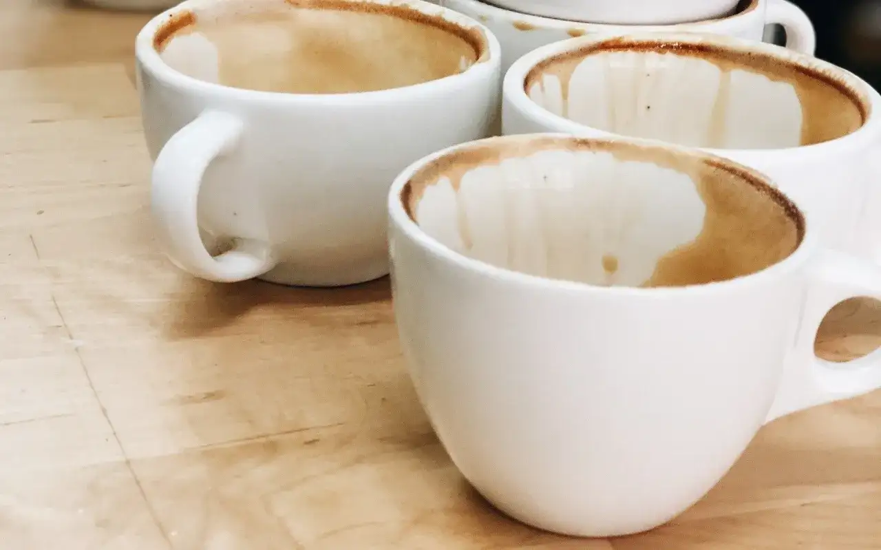 Kilka białych filiżanek po herbacie z osadem na dnie i ściankach, stojących na drewnianym blacie.