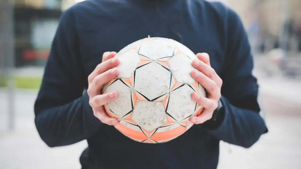 Osoba trzymająca w dłoniach zniszczoną piłkę nożną.