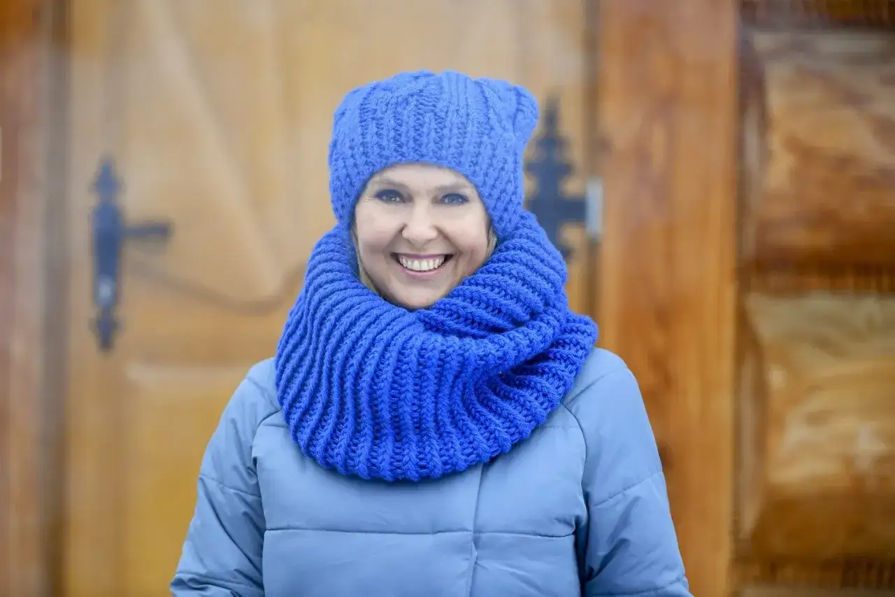 Uśmiechnięta kobieta w niebieskiej czapce i szaliku, idealny przykład, jak dobrać czapkę do płaszcza.