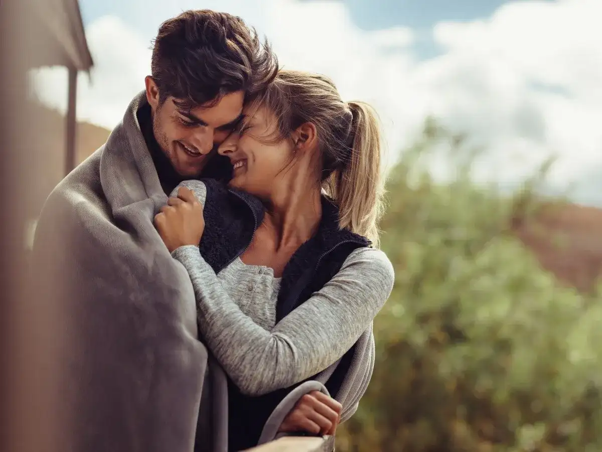 Para zakochanych przytulająca się pod kocem na tle natury.