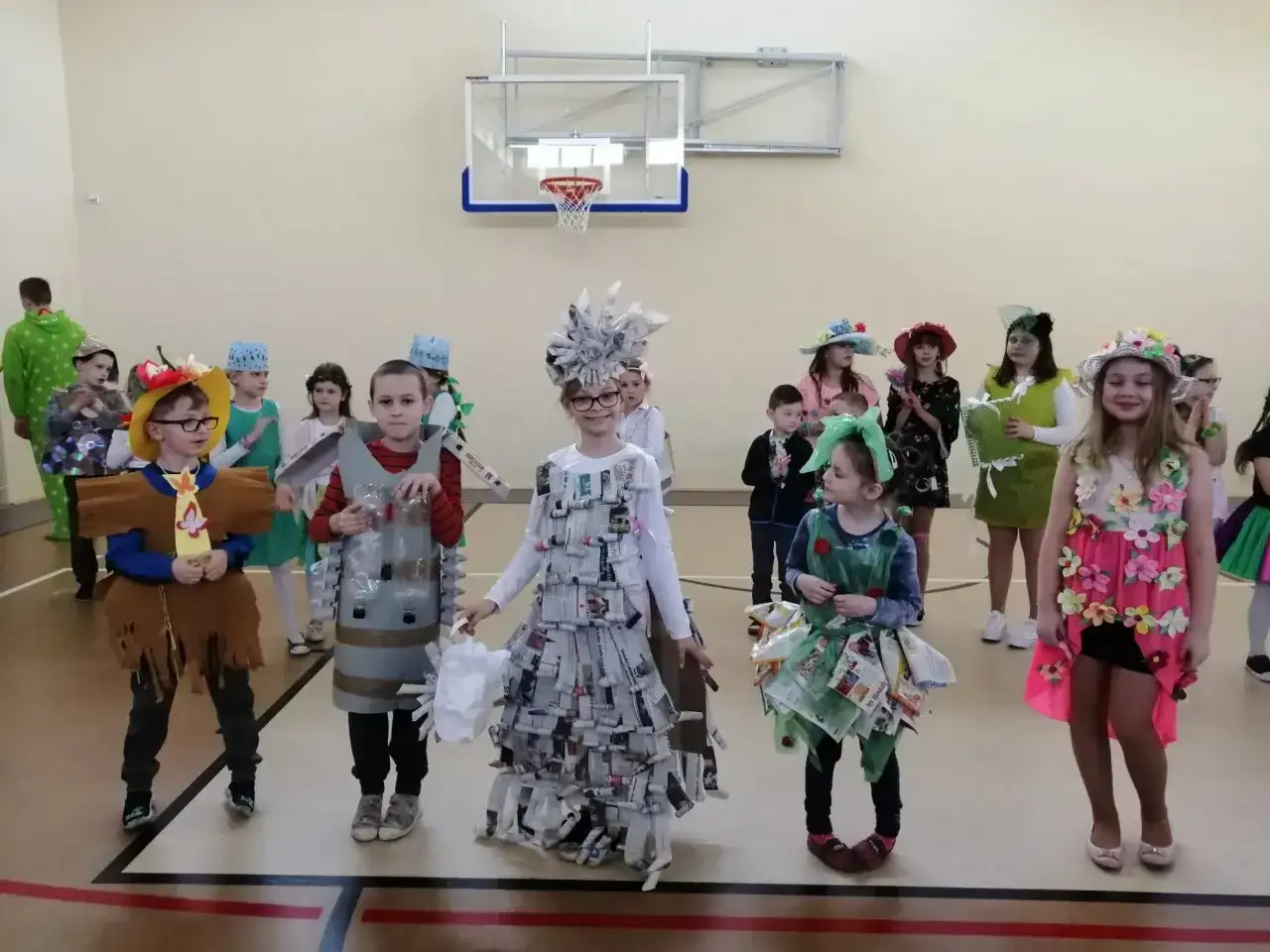 Dzieci prezentują stroje na Dzień Wiosny. Chłopiec w brązowym stroju z frędzlami, obok niego chłopiec w stroju z butelek.