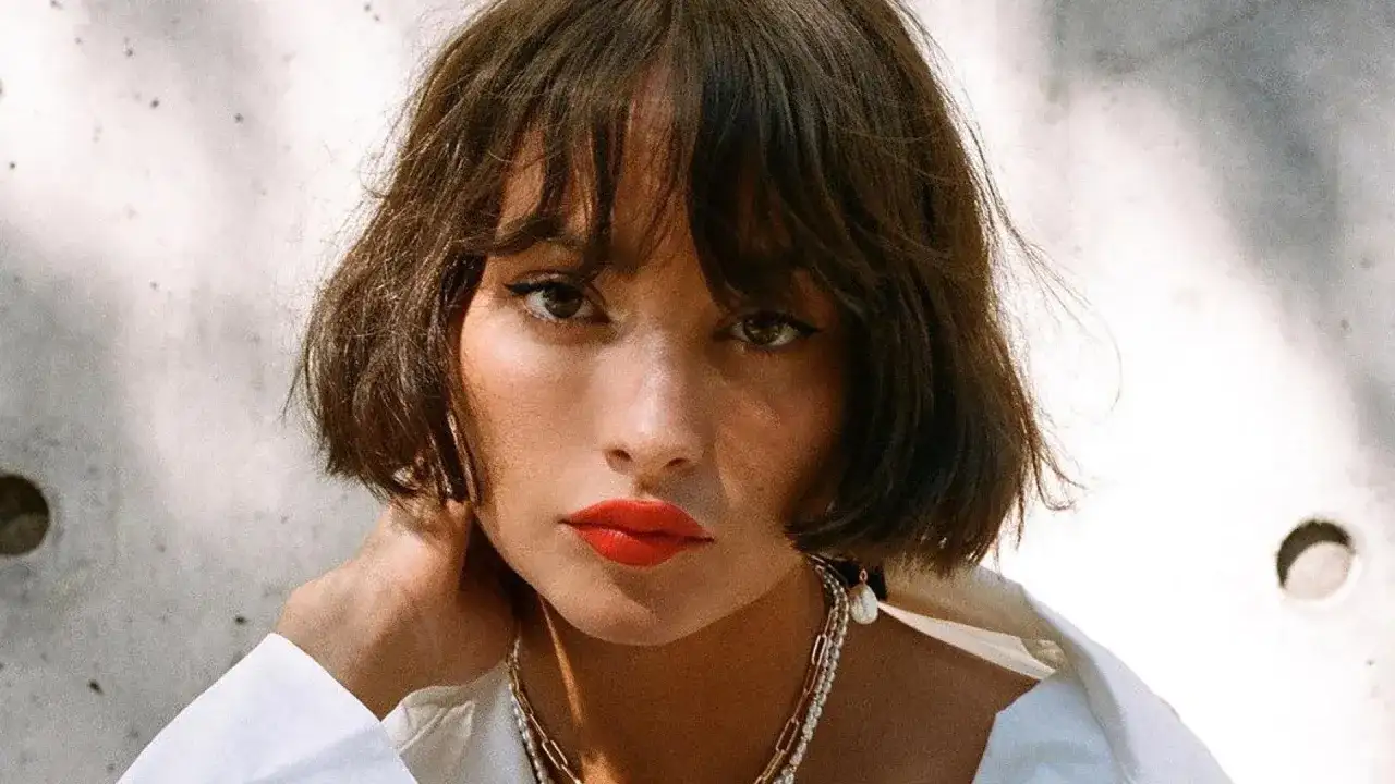 Krótkie, falowane włosy z grzywką to idealna fryzura do wysokiego czoła. Modelka ma wyraziste usta i delikatną biżuterię.