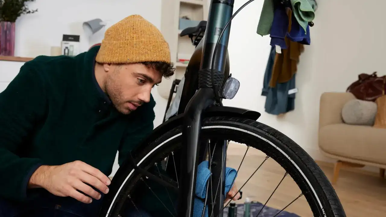 Mężczyzna w czapce czyści rowerową obręcz niebieską ściereczką.