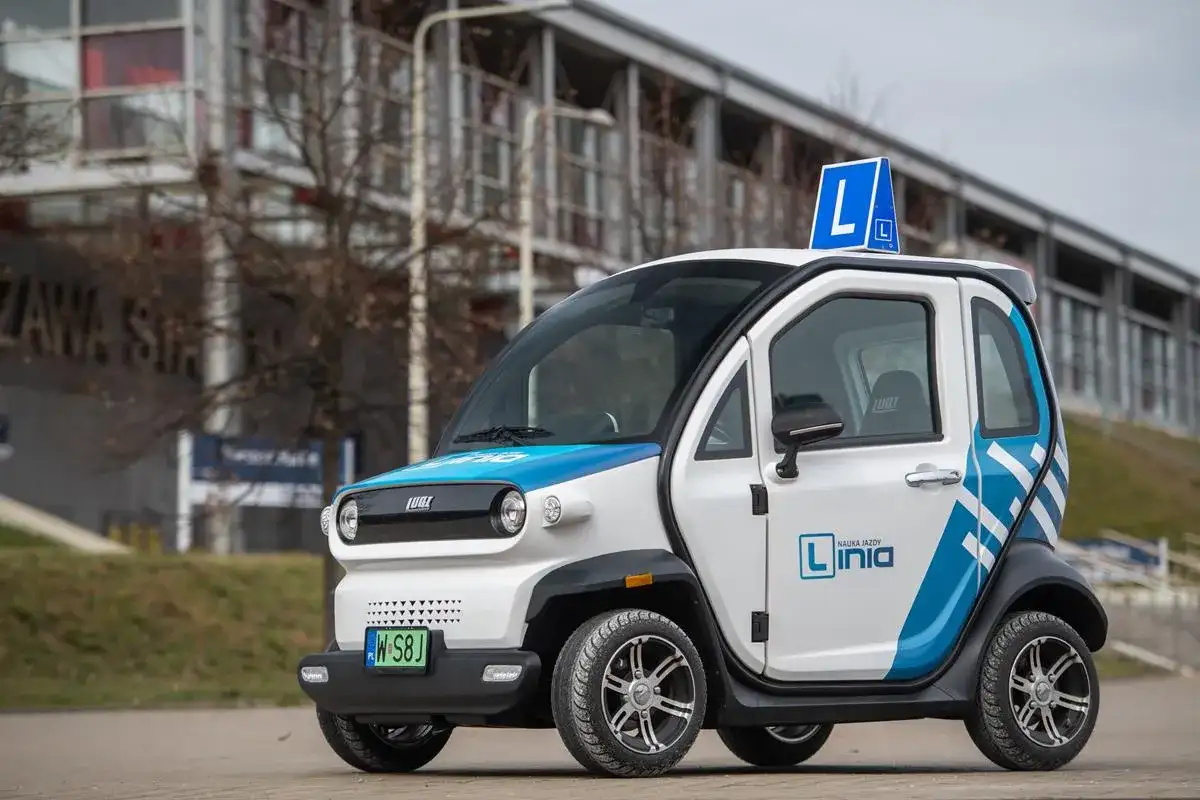 Mały, biało-niebieski pojazd samochodowy inny niż typowe auto, z literą "L" na dachu, idealny do nauki jazdy.