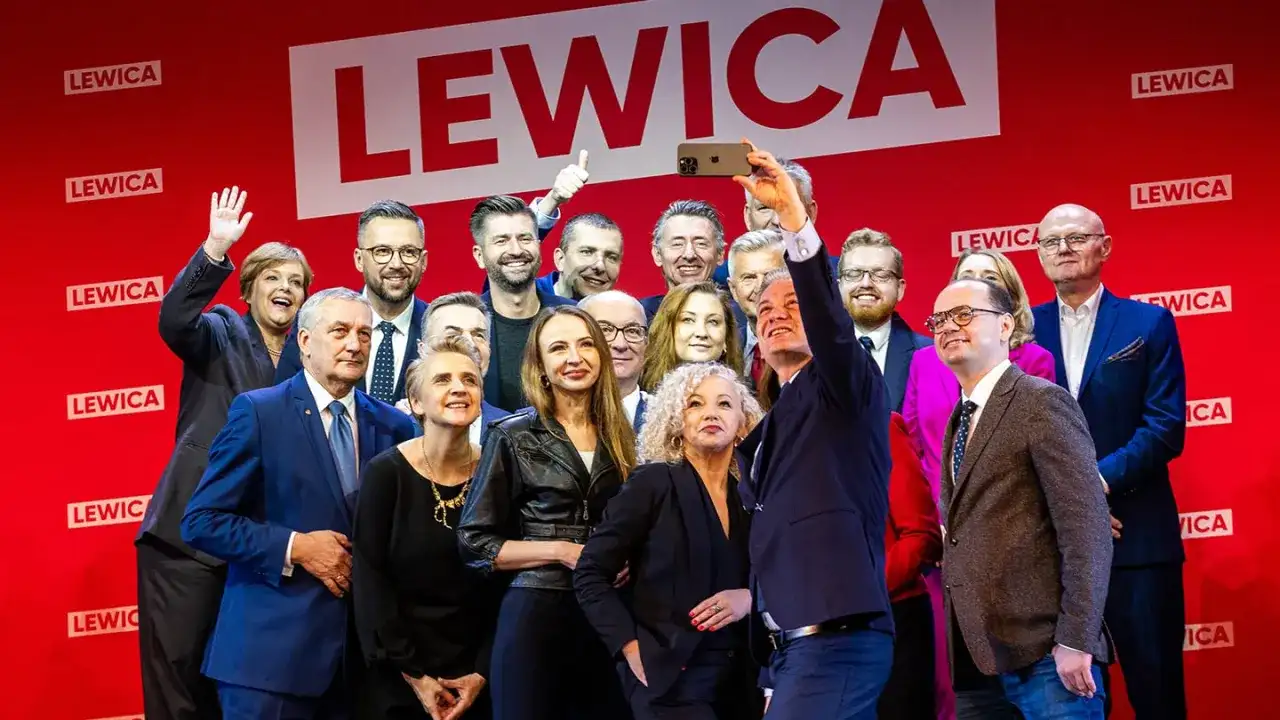 Grupa polityków Lewicy pozuje do selfie na tle czerwonej ściany z logo partii.