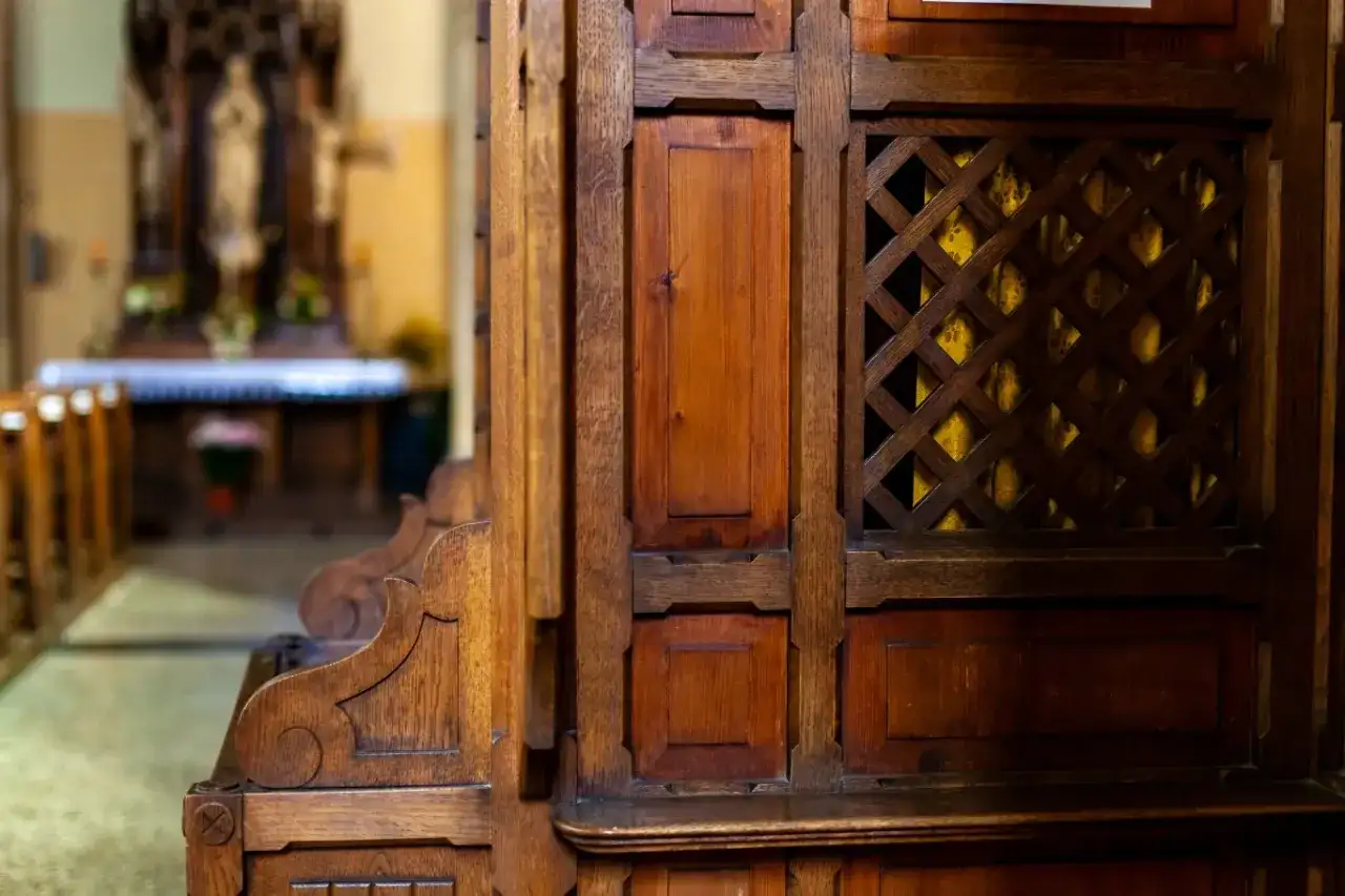 Drewniana konfesjonał w kościele, z widocznym kratkowanym okienkiem i wnętrzem.