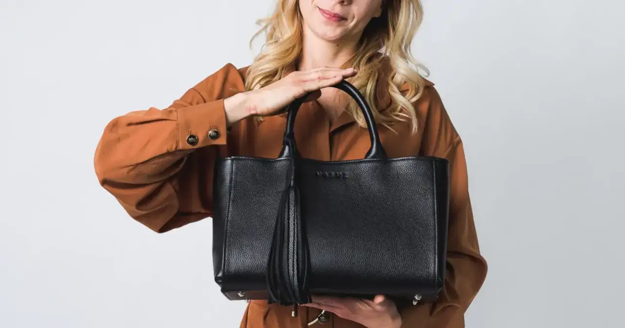 Elegancka, czarna torebka z frędzlem, idealna jako modne torebki na lato. Kobieta w rudym kombinezonie prezentuje stylowy dodatek.