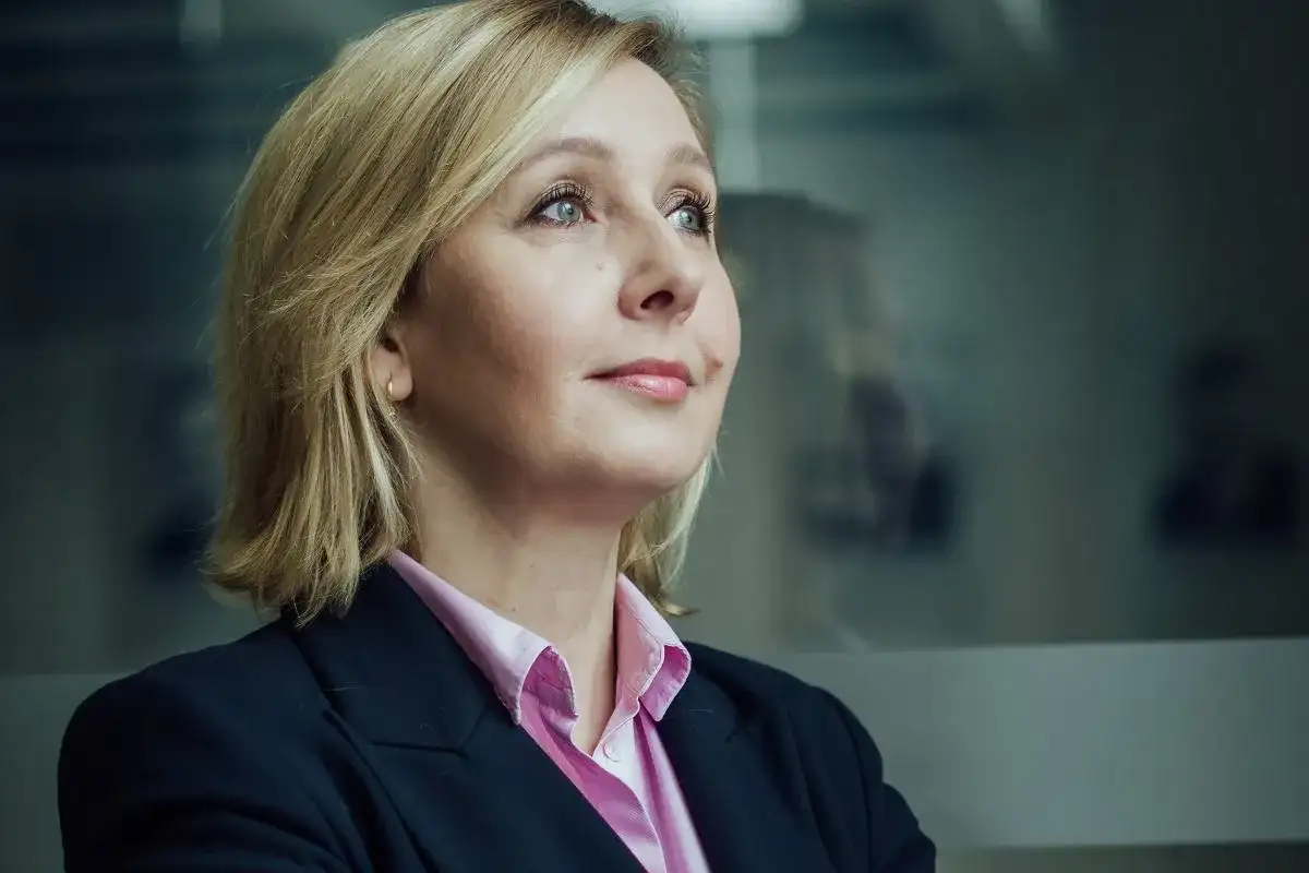Blond polityk w różowej koszuli i granatowej marynarce patrzy w bok. W tle rozmyte sylwetki innych polityków.
