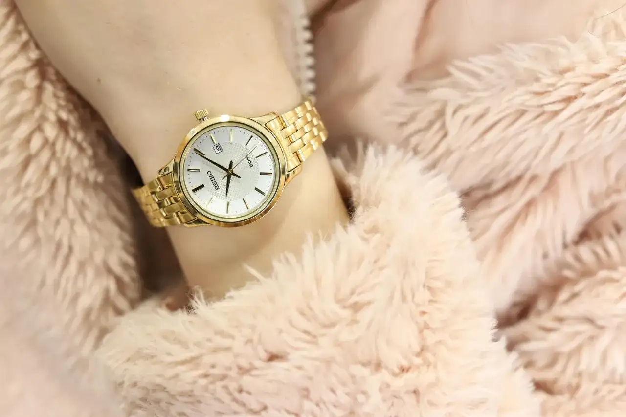 Złoty zegarek damski Seiko na nadgarstku, otoczony różowym futerkiem.