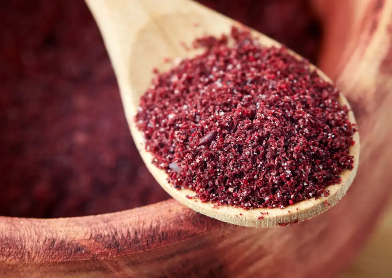 Drewniana łyżka z mielonym sumakiem, idealną przyprawą do dań kuchni bliskowschodniej. Gdzie kupić sumak? W sklepach z przyprawami i online.