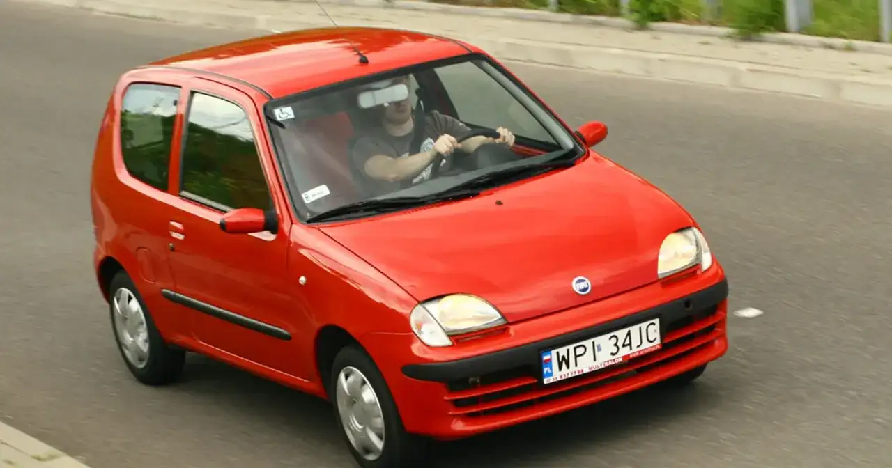 Czerwone Fiat Seicento w ruchu drogowym, widok z przodu i z boku.