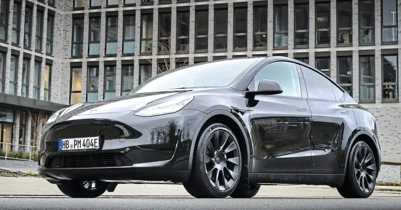 Czarny Tesla Model Y stoi przed nowoczesnym budynkiem z cegły.