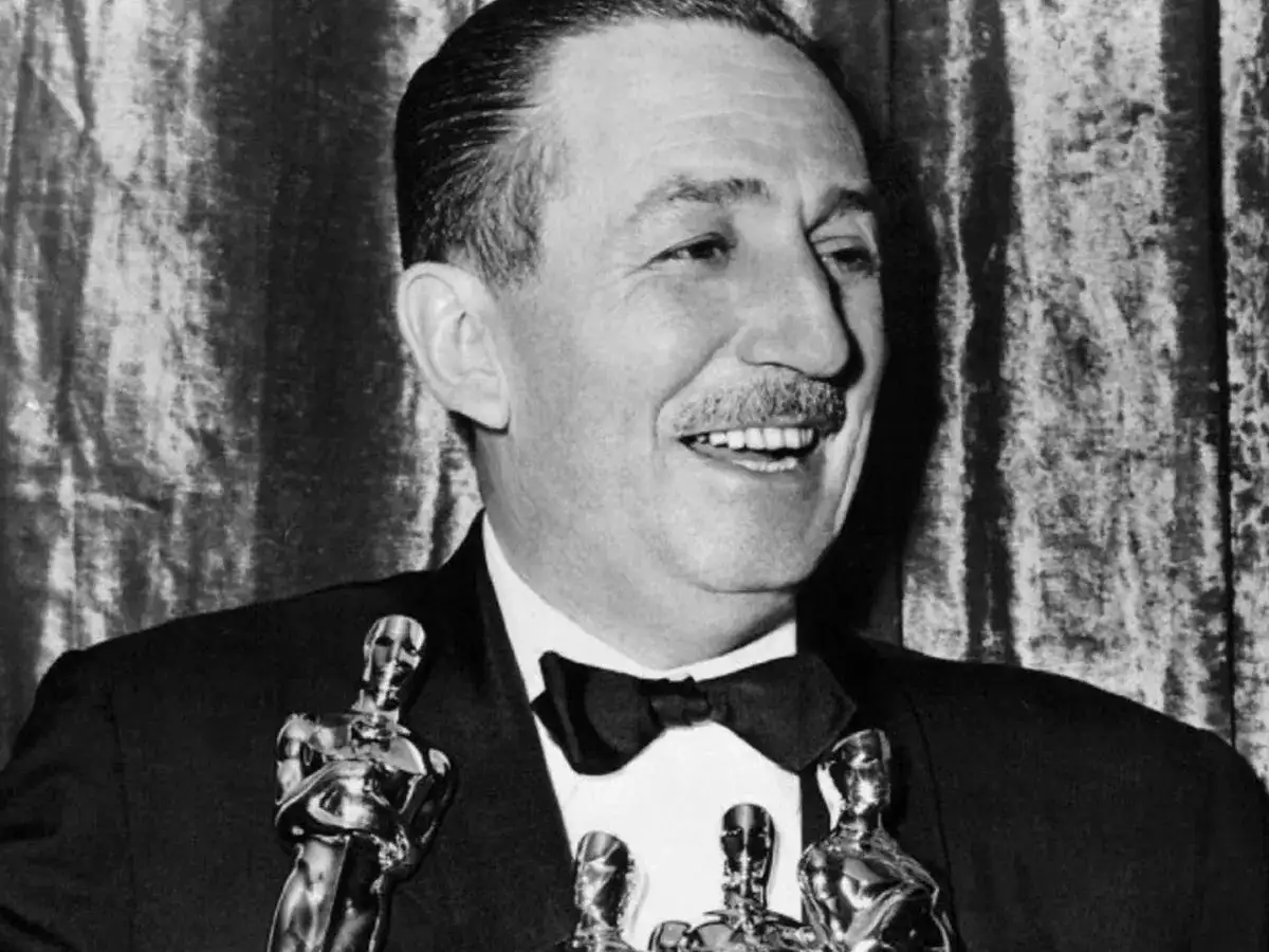 Walt Disney, który zdobył najwięcej Oscarów, uśmiecha się, trzymając statuetki.