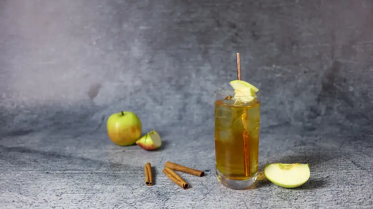 Szklanka z drinkiem, jabłka, laska cynamonu na szarym tle.