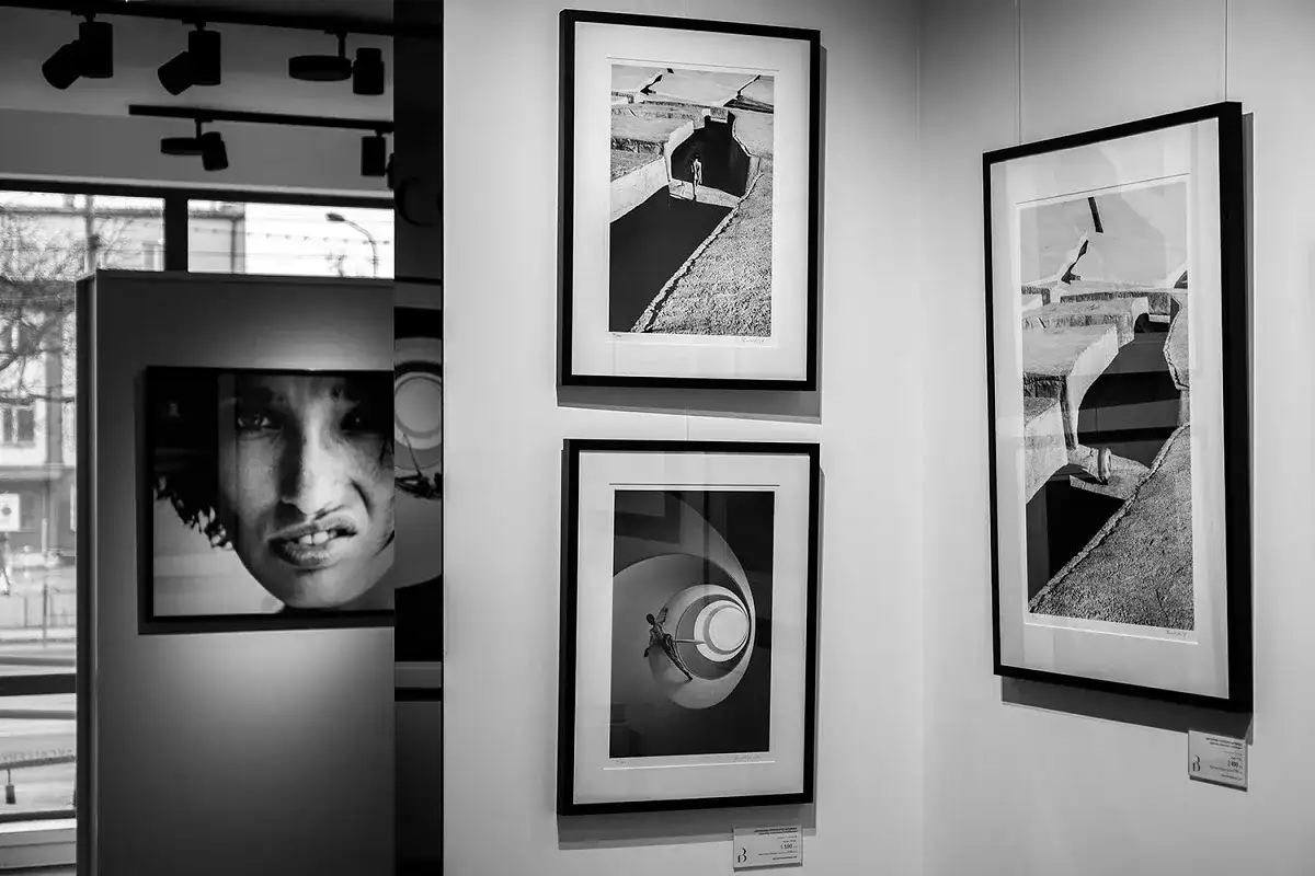 Wystawa prac fotografa. Różne rozmiary zdjęć: portret kobiety, postać w kanale, schody spiralne.