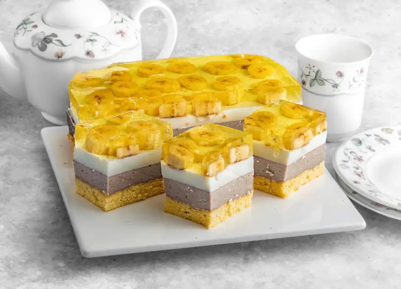 Pyszne bananowiec ciasto z galaretką i bananami, pokrojone na porcje. Obok czajniczek i filiżanka.